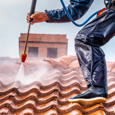 Worker pressure-washing a terracotta roof with a red nozzle and blue hose