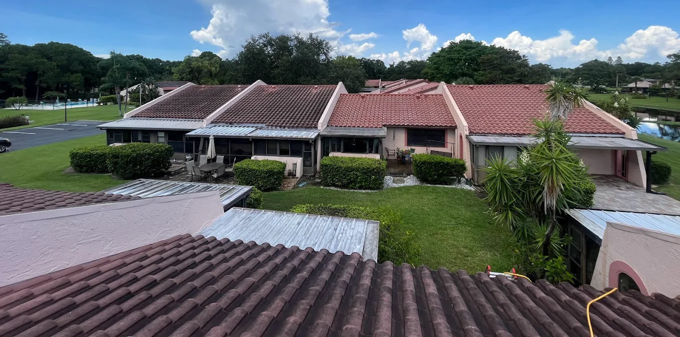 Aerial view of a row of red-tiled houses with lawns and a driveway under a partly cloudy sky.