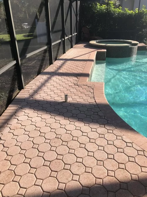 Screened pool deck with pink pavers, turquoise water, and a round spa in sunlight