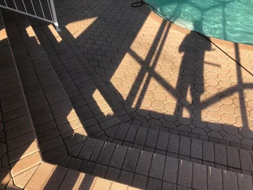 Shadows of a railing cast across a brick-paved walkway in warm sunlight.
