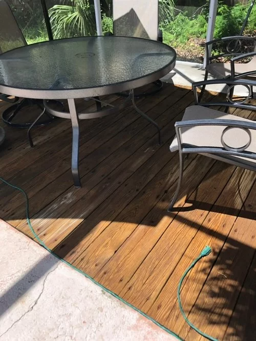 Patio with round glass table, metal chairs, wooden deck, and a hose on the ground
