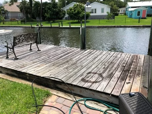 Wooden deck by a canal with a bench, grassy bank, and houses across the water