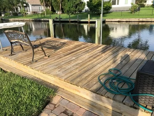 Wooden dock with a bench and coiled hose beside a calm canal lined with houses and trees