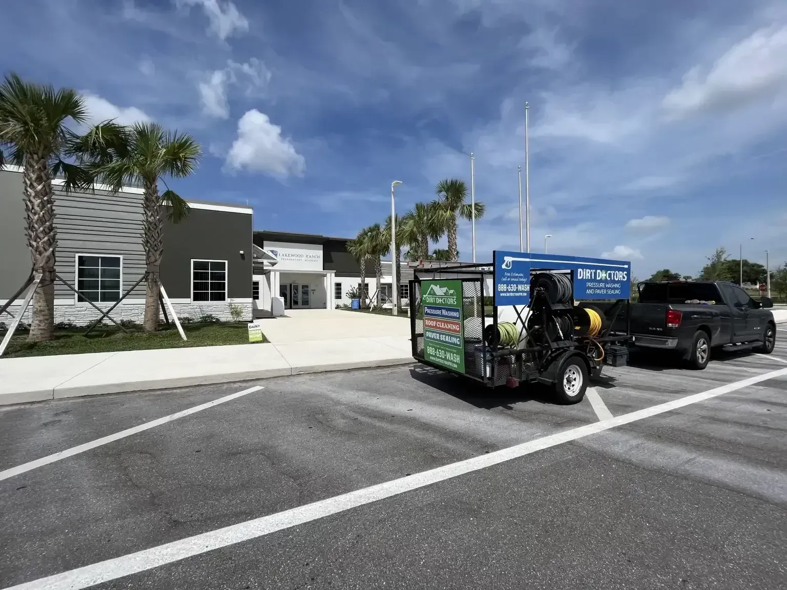 Advertising trailer parked beside a black pickup in a sunny parking lot outside a building.