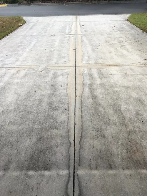 Concrete driveway with a long center crack leading to the street, bordered by grass.