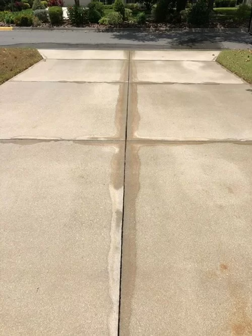 Concrete driveway with a long center crack leading to a street and shrubs beyond