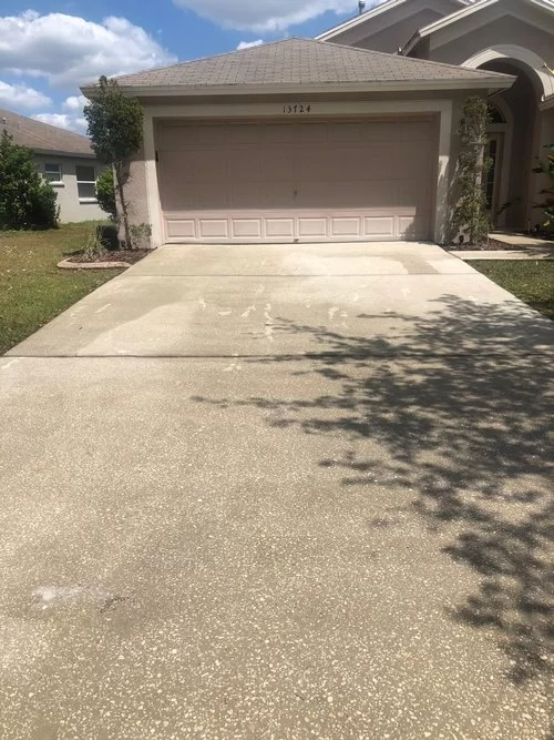 Suburban house with a two-car garage and a long concrete driveway under a partly cloudy sky