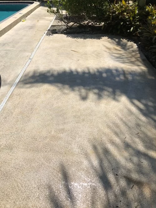 Sunlit concrete poolside walkway with shadows and landscaping beside the water