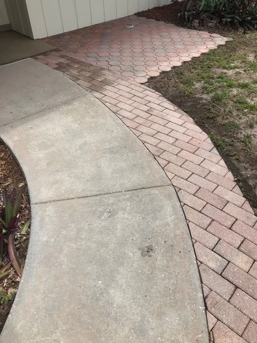 Curved concrete walkway beside a brick border and patchy grass in a yard