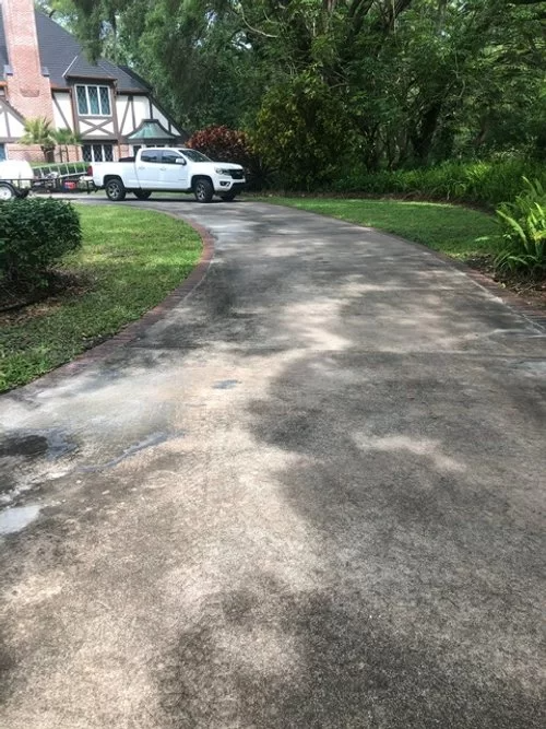Curved driveway beside a house and trees, with a white pickup truck parked near the entrance.