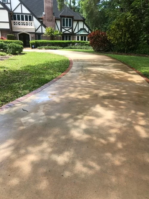 Curved concrete walkway leading to a Tudor-style house with green lawn and trees