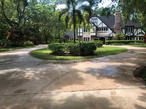 Curved driveway leading to a Tudor-style house surrounded by lush trees and landscaping