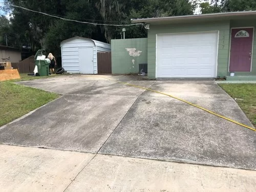 Driveway leading to a garage and shed; two people stand near trash bins on the left.