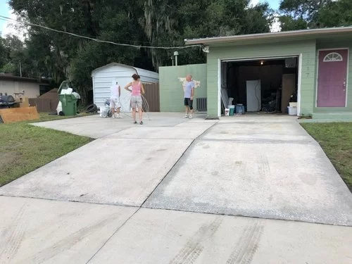 Residential driveway with two people standing near a garage and a small shed.