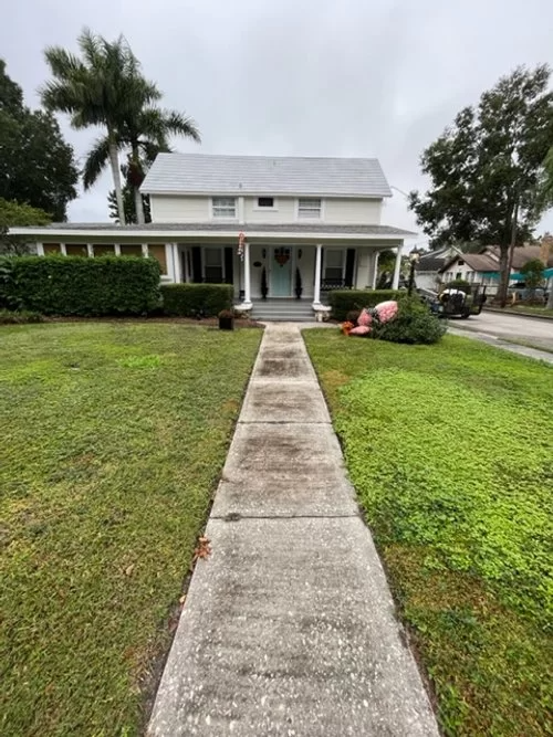 Concrete walkway leading to a white two-story house with a front porch and green lawn