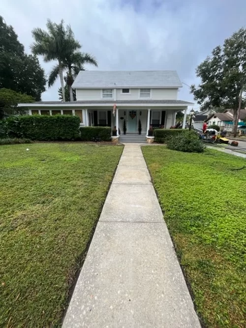 Front yard with a concrete walkway leading to a white house with a covered porch and green lawn