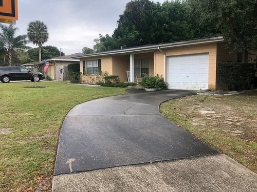 Single-story beige house with a curved black driveway and white garage door in a grassy suburban yard