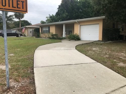 Curved concrete walkway leading to a beige building with a white garage door and grassy lawn