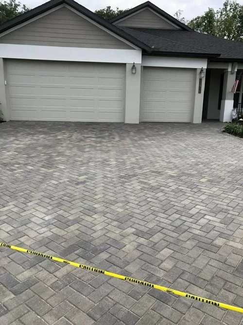 Paver driveway in front of a gray two-car garage, with yellow caution tape across the foreground.