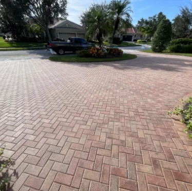 Brick-paved driveway leading to a suburban home, with a parked car and landscaped island.