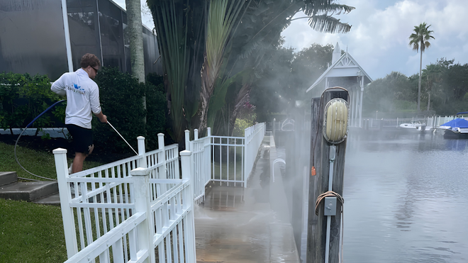 Storm surge flooding a waterfront walkway beside a white fence, with a person standing nearby.