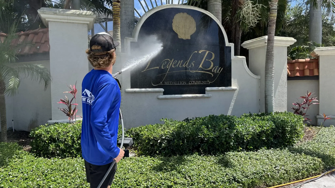 Person in blue shirt watering a memorial plaque in a landscaped garden.