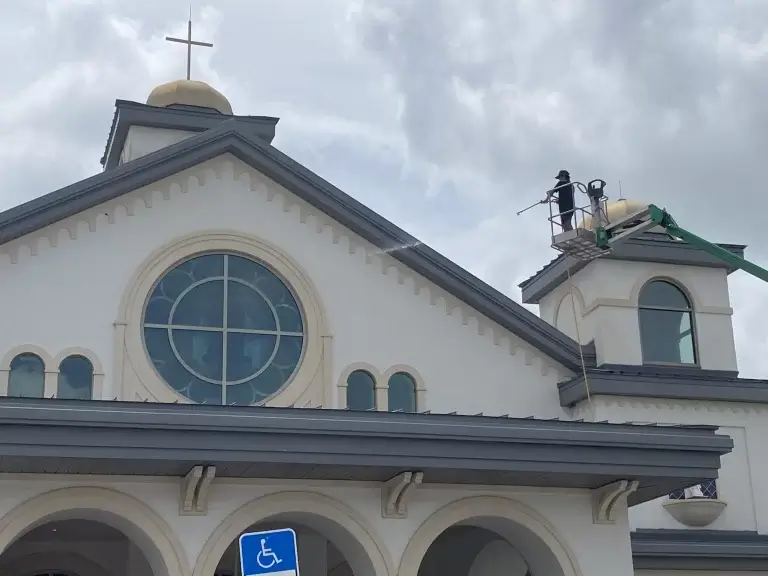 Church facade with circular window, cross, and accessible entrance sign under cloudy sk