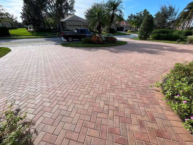 Brick-paved circular driveway in a landscaped neighborhood with trees and a gazebo.