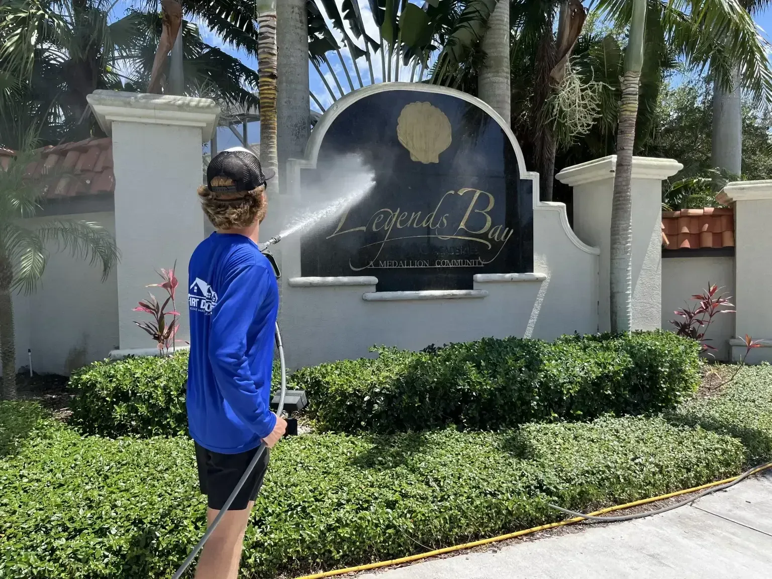 Person spraying water at a resort entrance sign surrounded by palm trees and shrubs