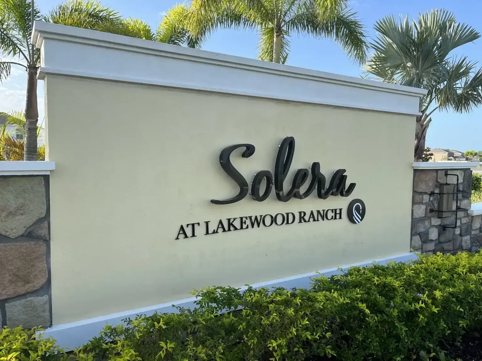 Solara at Lakewood Ranch entrance sign on a cream wall with palm trees and hedges behind it