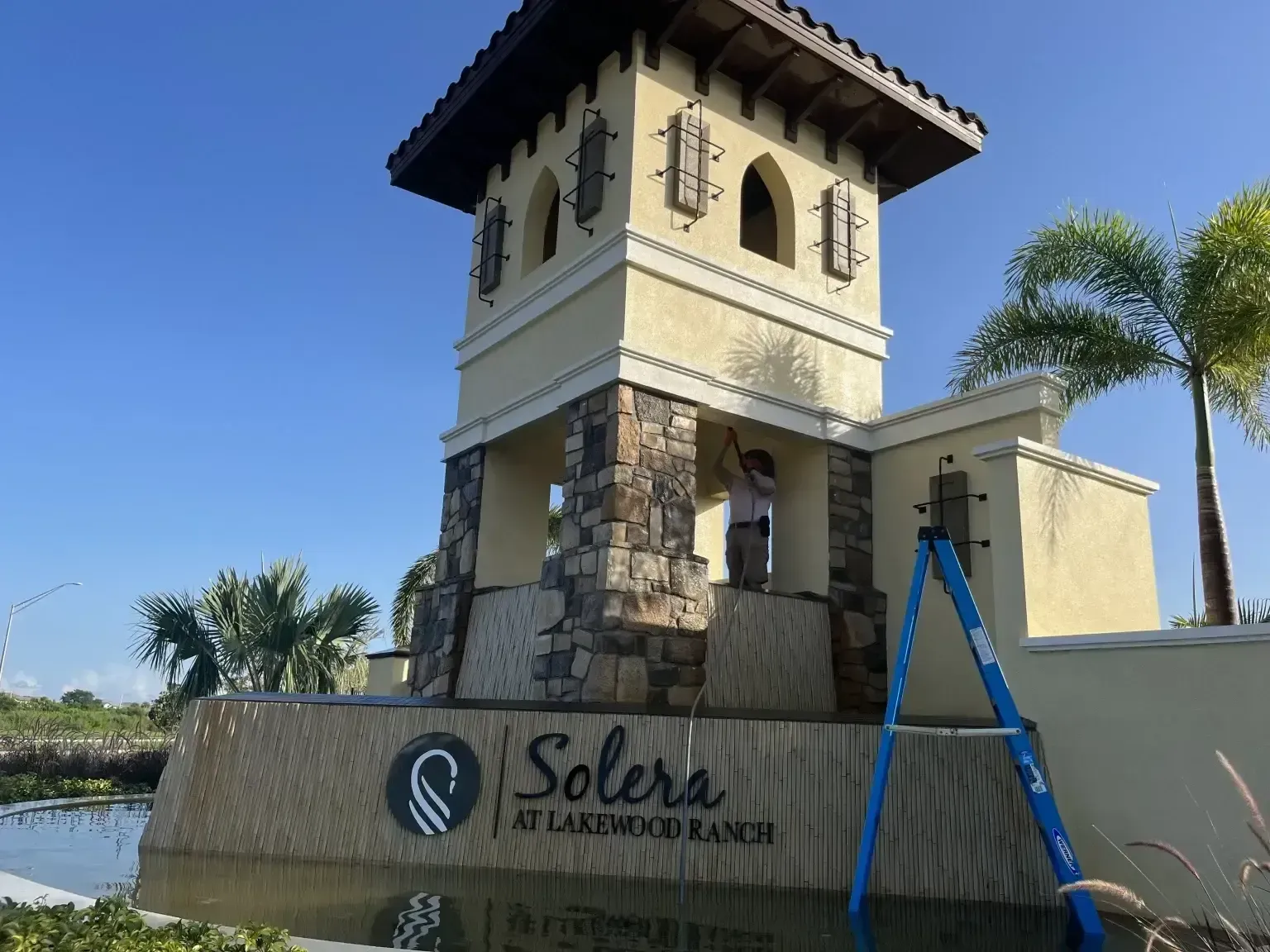 Palm-lined entrance tower with stone base and “Solera” sign under a clear blue sky.