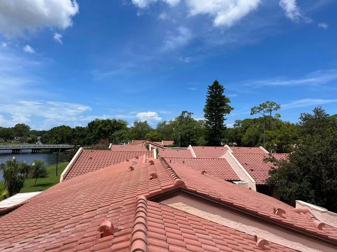 Terracotta-tiled rooftops beneath a bright blue sky with clouds, overlooking a river and trees