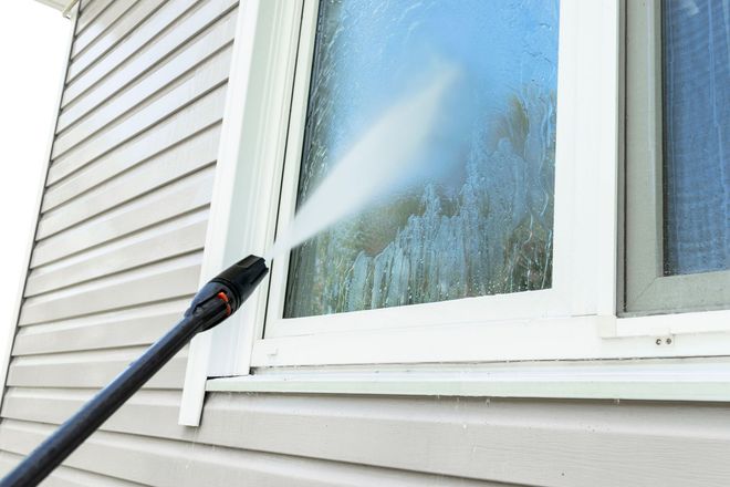 Pressure washer spraying a house window and siding with water