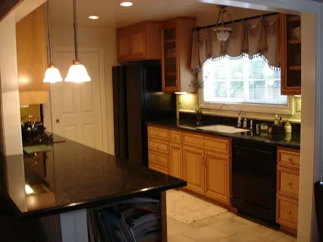 Kitchen with light-brown cabinets, black appliances, and granite countertops. Two pendant lights hang over a dark island.
