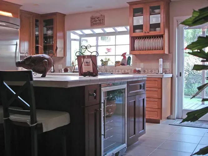 Kitchen with wooden cabinets, island with wine fridge, and outdoor view.