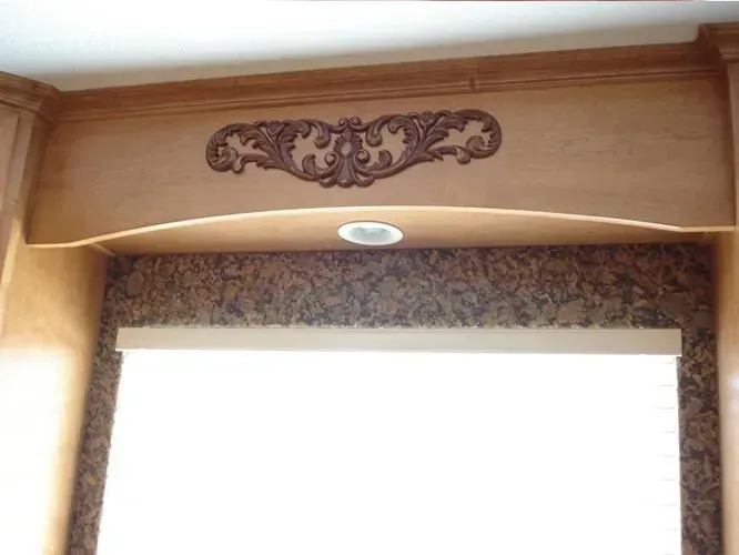 Wooden kitchen cabinets with a decorative scroll above a window.