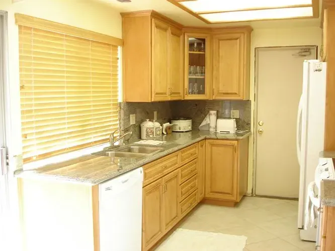 Kitchen with light wood cabinets, stainless steel sink, granite countertops, and a white refrigerator.