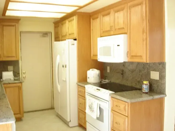 Kitchen with light wood cabinets, white appliances, and gray countertops.