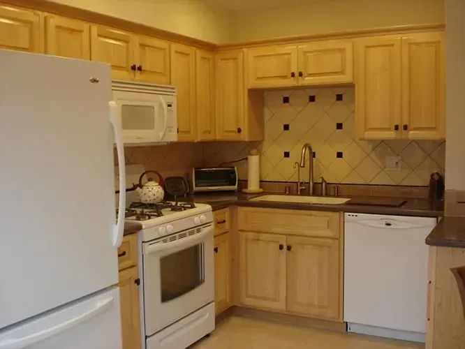 Kitchen with light wood cabinets, white appliances, and tiled backsplash.