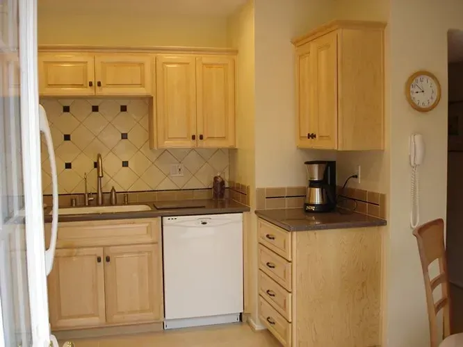 Small kitchen with light wood cabinets, white dishwasher, and coffee maker on the counter.