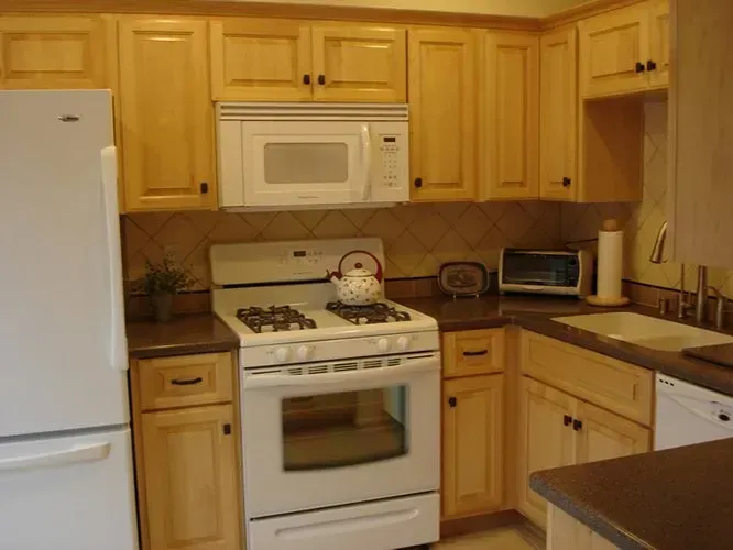 Kitchen with light wood cabinets, white appliances, and a dark countertop.