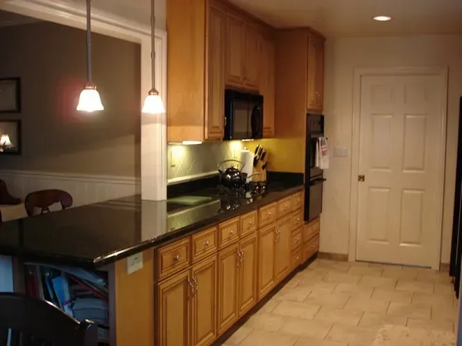 Kitchen with light wood cabinets, dark countertop, and built-in appliances, next to a door.