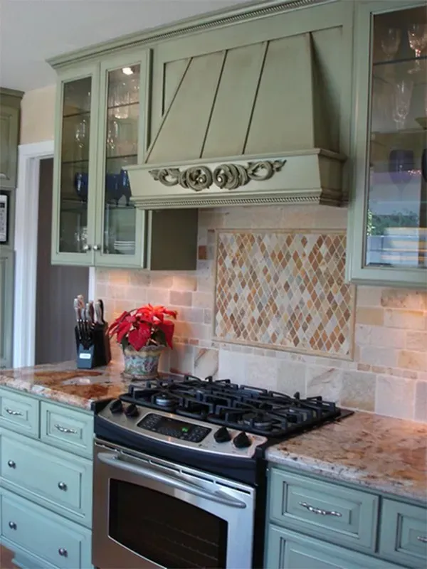 Green kitchen with range, tiled backsplash, and decorative hood.
