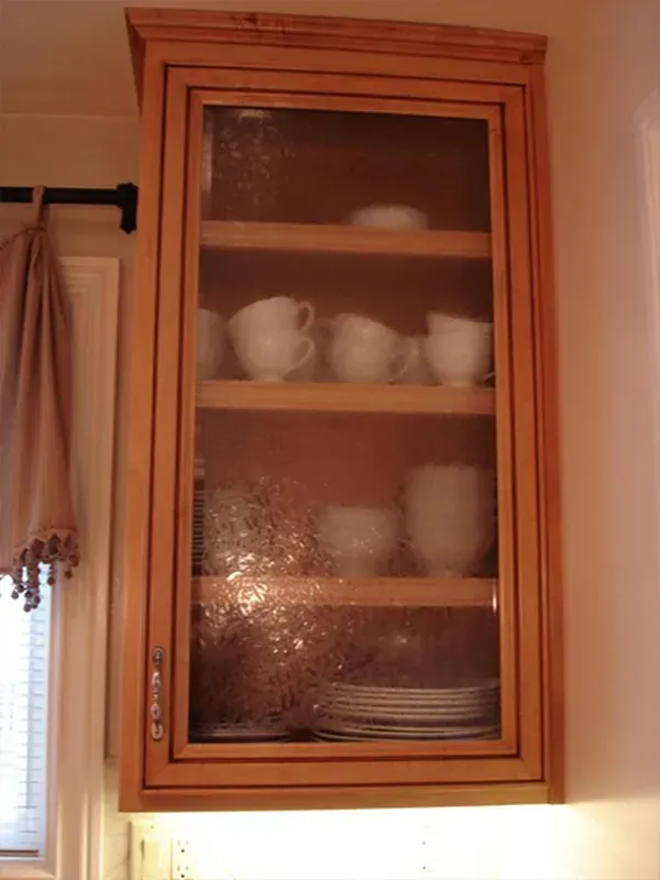 Wooden kitchen cabinet with glass door, displaying white dishes.