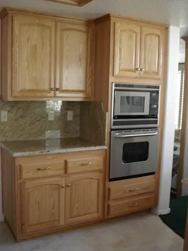 Light wood kitchen cabinets with built-in microwave and oven, granite countertop, backsplash.