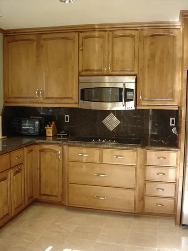 Kitchen with light wood cabinets, stainless steel microwave, black backsplash, and tile floor.