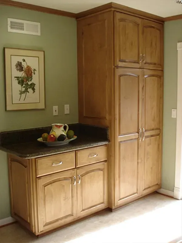 Kitchen corner with light brown cabinets, dark countertop, olive green wall, framed artwork.