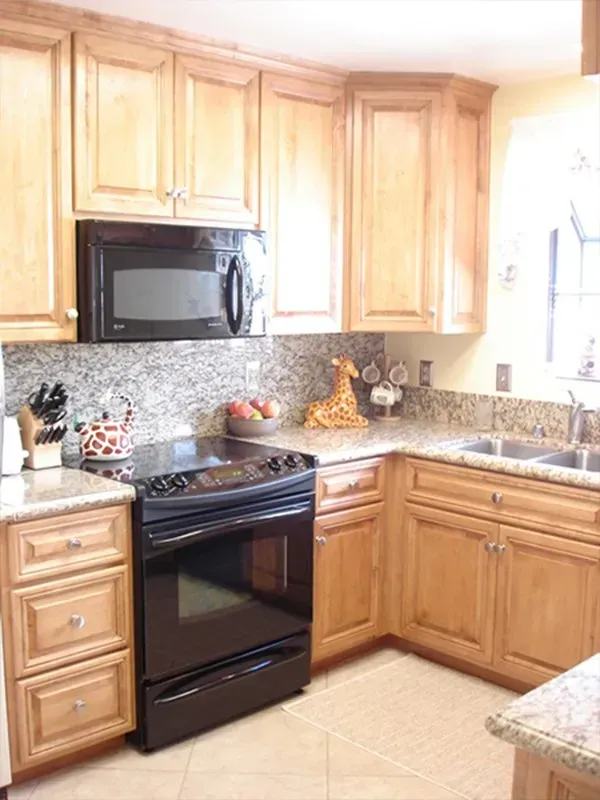 Kitchen corner with light brown cabinets, black appliances, and granite countertops.