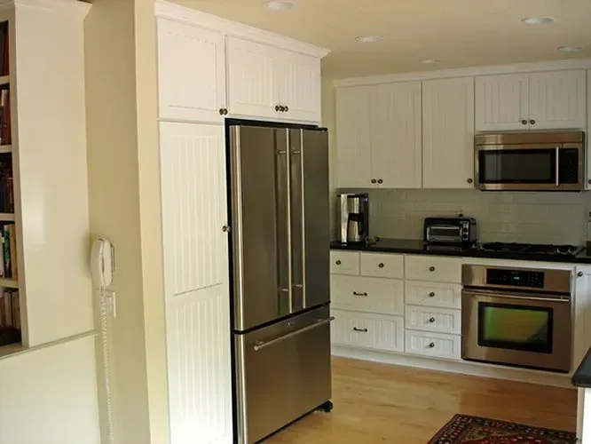 White kitchen with stainless steel appliances. Refrigerator and oven are focal points. Cabinets and walls are white.
