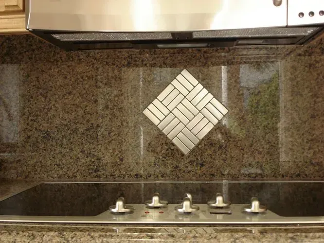 Brown granite backsplash with metal tile diamond pattern above a cooktop.